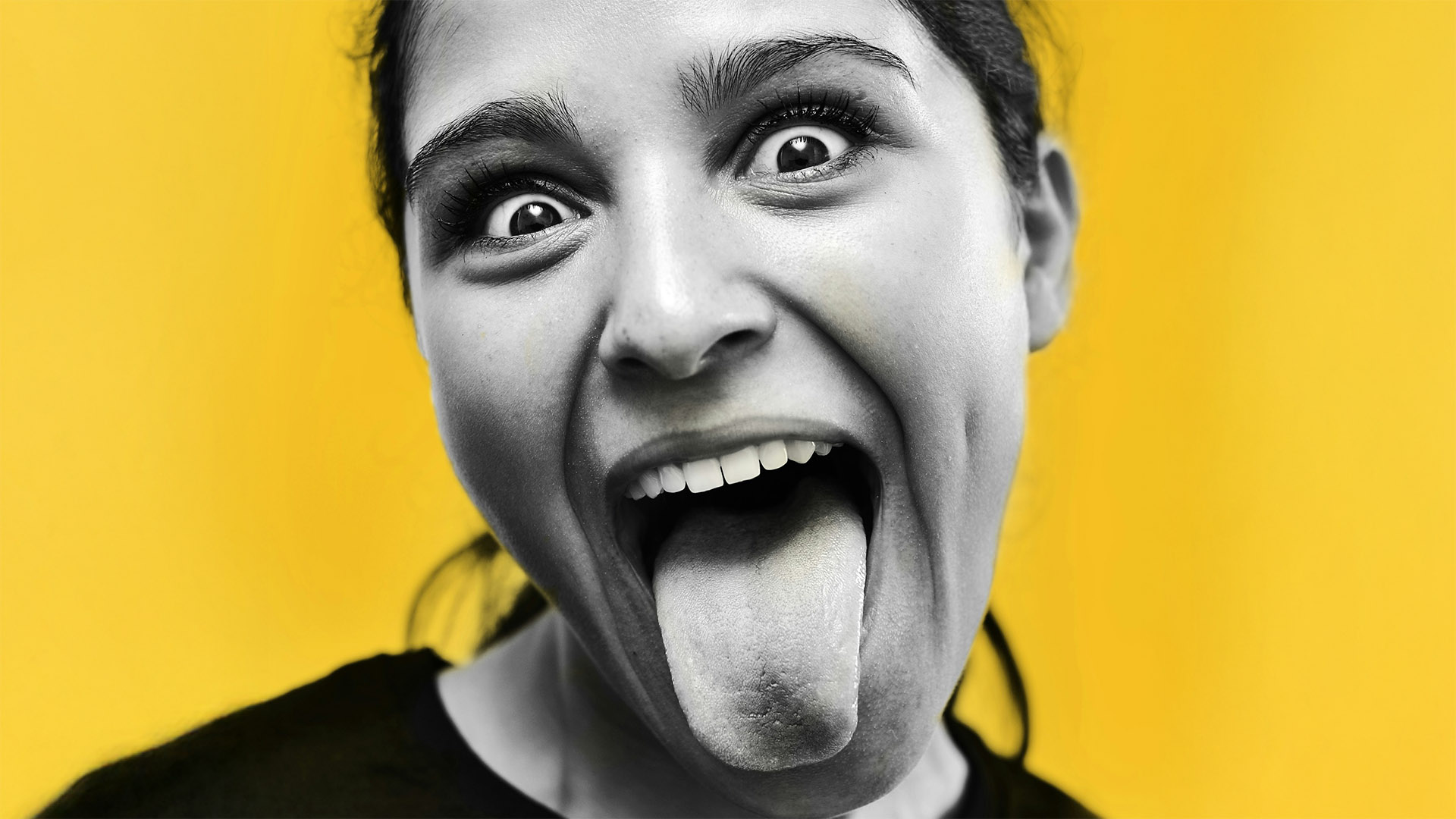 Meisje op gele achtergrond steekt tong uit.